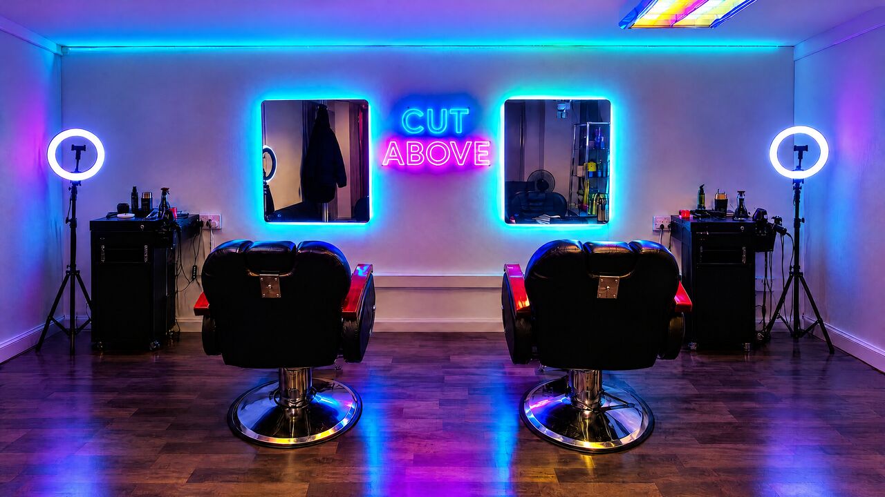 The shop at night: two barber chairs between ring lights under a neon sign